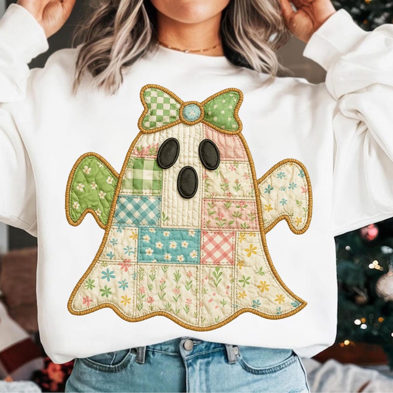 May include: White sweatshirt featuring a patchwork ghost design. The ghost has a green bow, black oval eyes, and a patchwork body with floral and plaid patterns in pastel colors. The design is outlined with a brown stitched border.