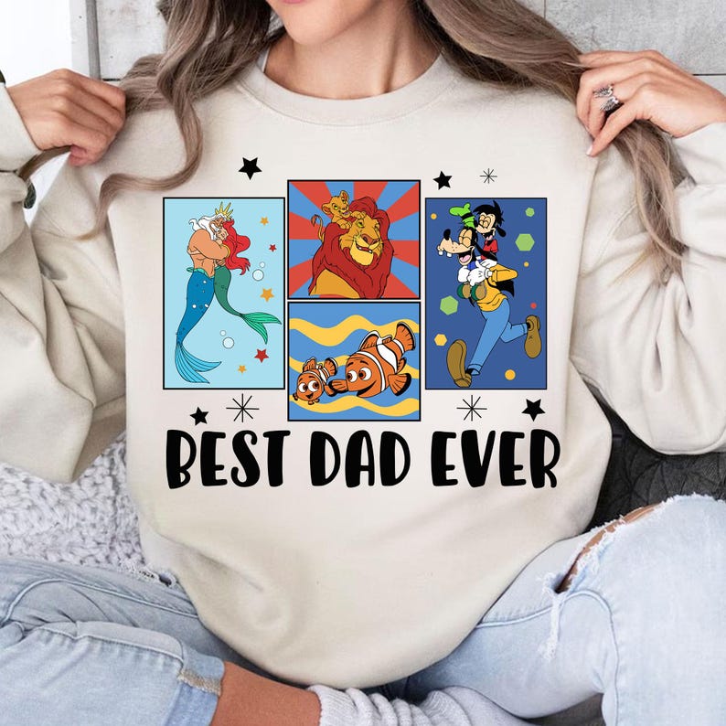 Pu&ograve; includere: Felpa color crema con un design grafico con personaggi dei cartoni animati Disney. Il design include Ariel, Simba, Nemo e Pippo, con la scritta "Best Dad Ever" in nero.