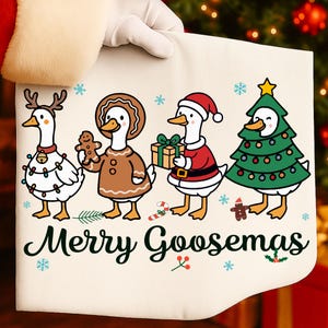 Peut inclure: Un tissu cr&egrave;me festif avec quatre oies de dessin anim&eacute; habill&eacute;es pour No&euml;l. L'une porte un serre-t&ecirc;te en forme de bois de renne, une autre tient un bonhomme en pain d'&eacute;pices et une troisi&egrave;me un cadeau. La derni&egrave;re oie est un sapin de No&euml;l. Le texte "Merry Goosemas" est &eacute;crit en dessous.