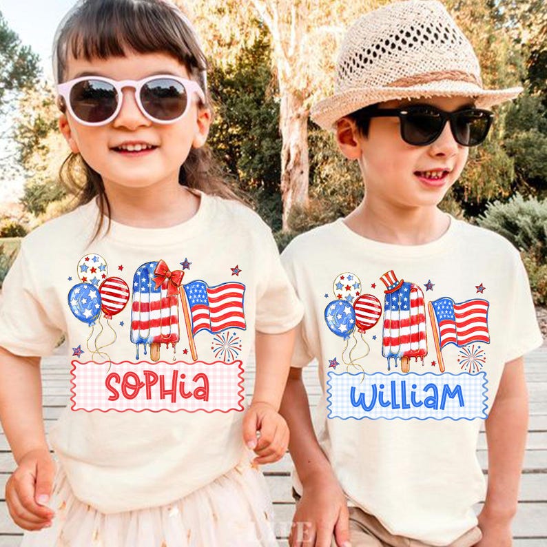 May include: Two children wearing cream-coloured t-shirts with patriotic designs. The shirts feature an American flag popsicle, balloons, and an American flag. One shirt says "Sophia" and the other says "William". Both children are wearing sunglasses.