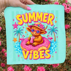 May include: A light blue square towel with the words "SUMMER VIBES" in yellow and pink. The design features a cartoon Highland cow wearing sunglasses and a hat, floating on a pink donut in water, with palm trees and flamingos.