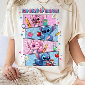 May include: Cream t-shirt with the text "100 Days of School" and a colourful graphic. The graphic features cartoon characters, pencils, apples, and books. Pink and blue stars and flowers are scattered around the design.