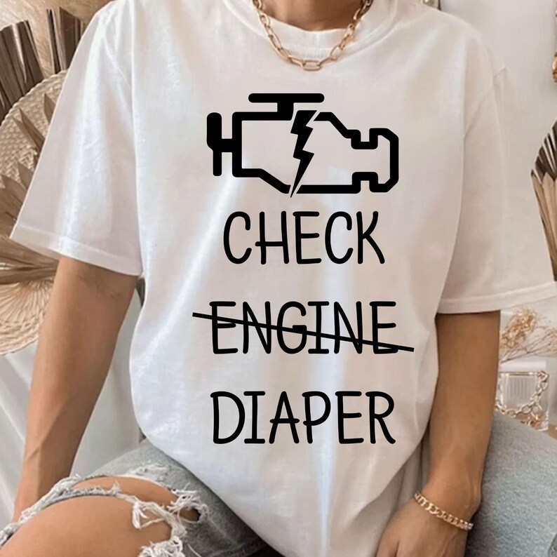 May include: White t-shirt with a black check engine light icon and the text "CHECK ENGINE DIAPER" with the word "ENGINE" crossed out.