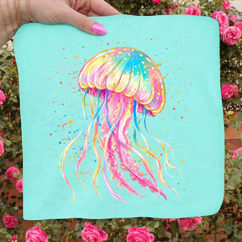 May include: A colorful jellyfish design on a light blue background. The jellyfish is painted with vibrant hues of pink, yellow, blue, and orange, with long, flowing tentacles. The design is on a square fabric, possibly a towel or pillow.