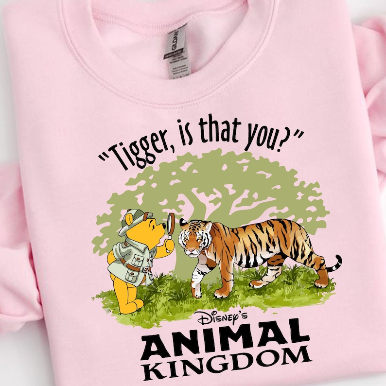 Puede incluir: Sudadera rosa con una imagen de dibujos animados de Winnie de Pooh mirando a un tigre a trav&eacute;s de una lupa. El texto "Tigger, is that you?" est&aacute; por encima de la imagen y "Disney's Animal Kingdom" est&aacute; por debajo de la imagen.