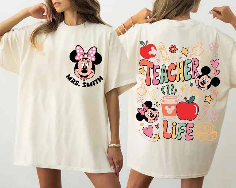 May include: Cream-coloured t-shirt with a Minnie Mouse design and the text "Mrs. Smith" on the front. The back features "Teacher Life" with school-themed graphics, including apples, pencils, and Mickey Mouse.