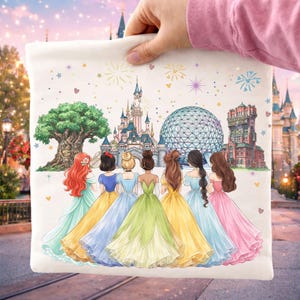 May include: A white tote bag featuring an illustration of six princesses in colorful gowns, facing away from the viewer, with iconic theme park landmarks in the background. Fireworks and stars decorate the sky.