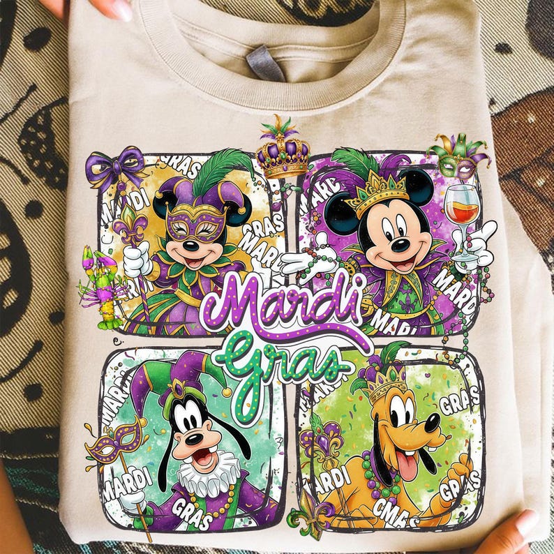 May include: Beige t-shirt featuring a colorful Mardi Gras design. The design includes Mickey Mouse, Minnie Mouse, Goofy, and Pluto in festive attire, with the words "Mardi Gras" prominently displayed.