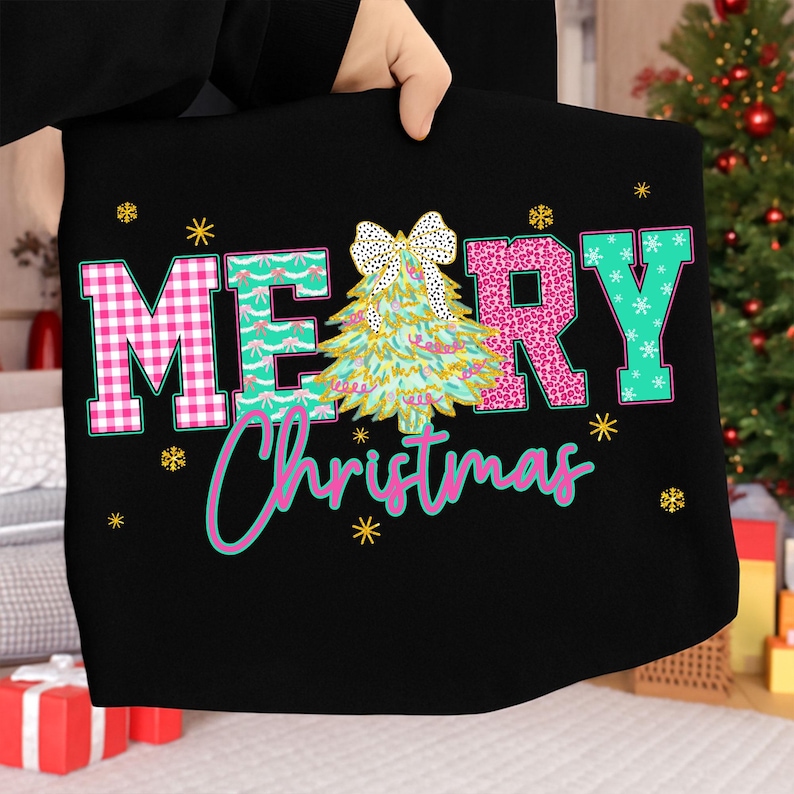 Puede incluir: Bolso tote negro con las palabras "MERRY Christmas" en un dise&ntilde;o colorido. Las letras son rosas, turquesas y blancas, con un &aacute;rbol de Navidad y un lazo en el centro. Estrellas doradas est&aacute;n dispersas alrededor del texto.