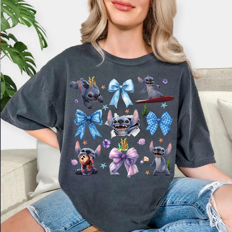 May include: Dark gray t-shirt featuring a collage of Stitch illustrations with blue bows, starfish, and floral accents. The design includes Stitch surfing, wearing a crown, and peeking through a torn paper effect. The shirt is a comfortable, casual wear.
