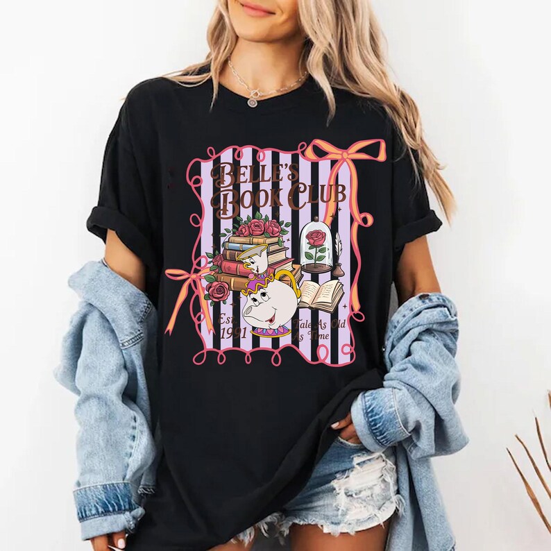 May include: Black t-shirt with a Belle's Book Club graphic. The design includes books, roses, a teapot, and the text "Tales As Old As Time." The shirt has a pink and purple striped background with pink bows and the text "Est. 1991."