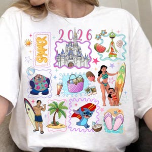 May include: White t-shirt with a colorful summer-themed graphic. The design includes illustrations of a castle, characters, a surfboard, and the text "Summer 2026". The overall theme is a vacation or beach setting.