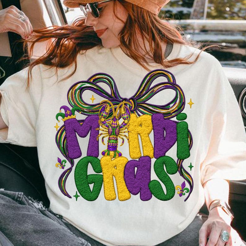 May include: Cream-colored sweatshirt with a vibrant Mardi Gras design. The graphic features the words "Mardi Gras" in purple, yellow, and green, with a lobster and bow detail. The design is festive and eye-catching.
