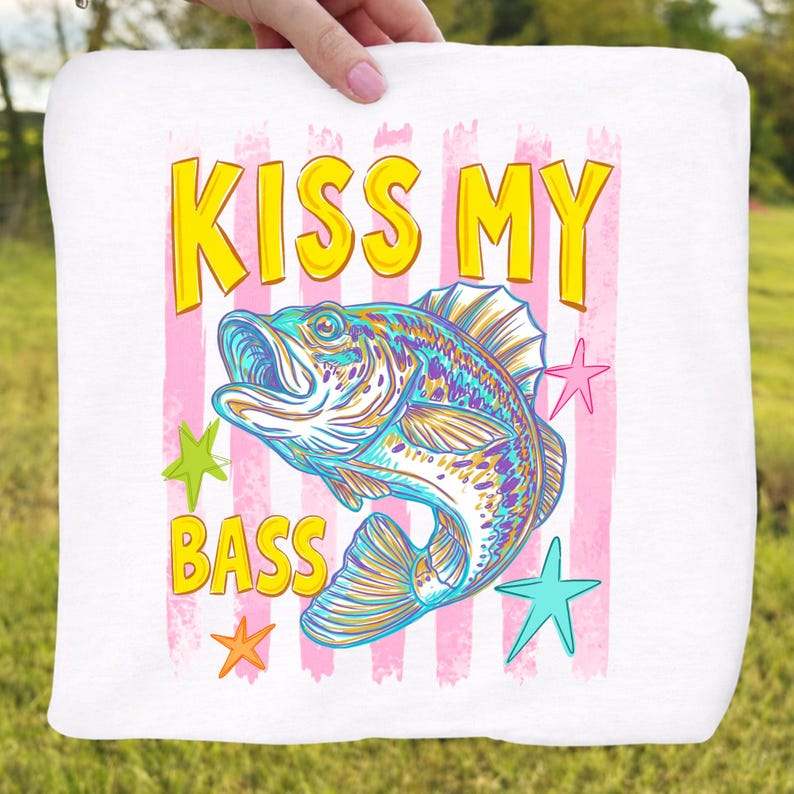 May include: White square fabric with the text "KISS MY BASS" in yellow and a colorful illustration of a fish. Pink vertical stripes and star shapes surround the fish. The fish is blue, yellow, and purple.