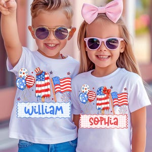 May include: Two children wearing white t-shirts with patriotic designs. The shirts feature an American flag popsicle, balloons, and the names "William" and "Sophia". Both children are wearing sunglasses and smiling.