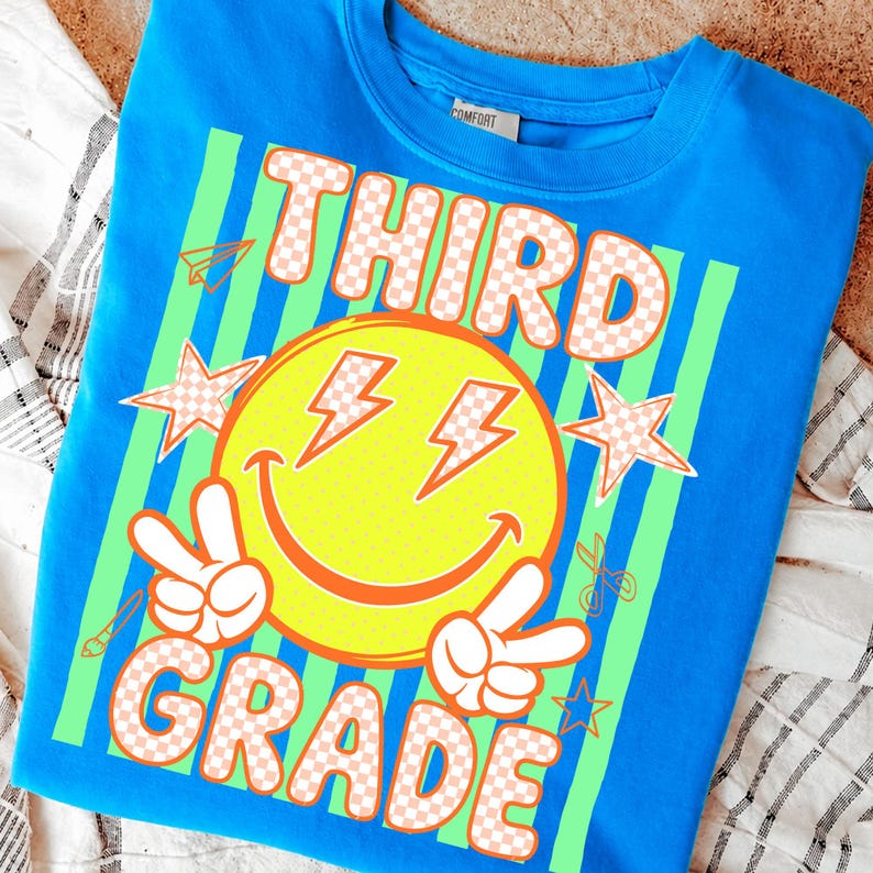 May include: A bright blue sweatshirt with a graphic design for third grade. The design features a yellow smiley face with lightning bolt eyes, peace signs, stars, and the words "THIRD GRADE" in a checkered pattern.