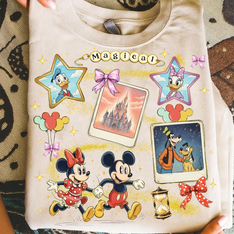 May include: Beige t-shirt featuring Disney characters and the word "Magical". The design includes images of Mickey and Minnie Mouse, Donald and Daisy Duck, Goofy and Pluto, and a castle. The shirt has a crew neck.