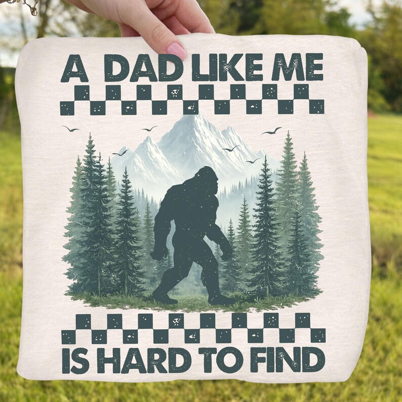 May include: A light-colored square blanket with the text "A DAD LIKE ME IS HARD TO FIND". The blanket features a Bigfoot silhouette in a forest scene with mountains and trees.