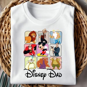 Pu&ograve; includere: T-shirt bianca con una griglia di illustrazioni di personaggi Disney, tra cui un leone, Topolino e altri. Le parole "Disney Dad" sono stampate in corsivo nero sotto la griglia.