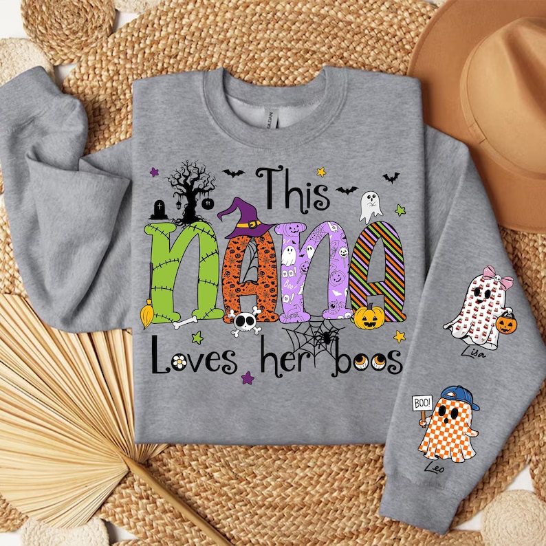 May include: A gray sweatshirt with the text "This Nana Loves her boos" in colorful Halloween-themed letters. The design includes ghosts, pumpkins, and a witch hat. The sleeves feature ghost graphics.