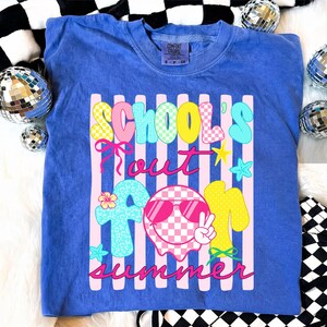 May include: A blue t-shirt with the words "SCHOOL'S OUT FOR SUMMER" in a colorful, playful font. The design includes a smiley face wearing sunglasses, stars, and a flower. The shirt is a Comfort Colors brand.