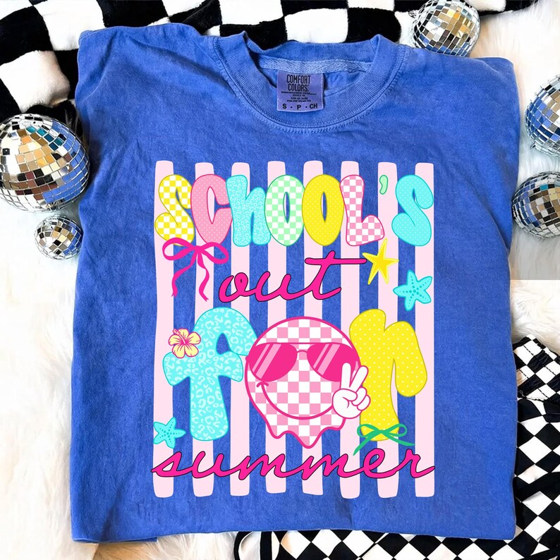 May include: A blue t-shirt with the words "SCHOOL'S OUT FOR SUMMER" in a colorful, playful font. The design includes a smiley face wearing sunglasses, stars, and a flower. The shirt is a Comfort Colors brand.