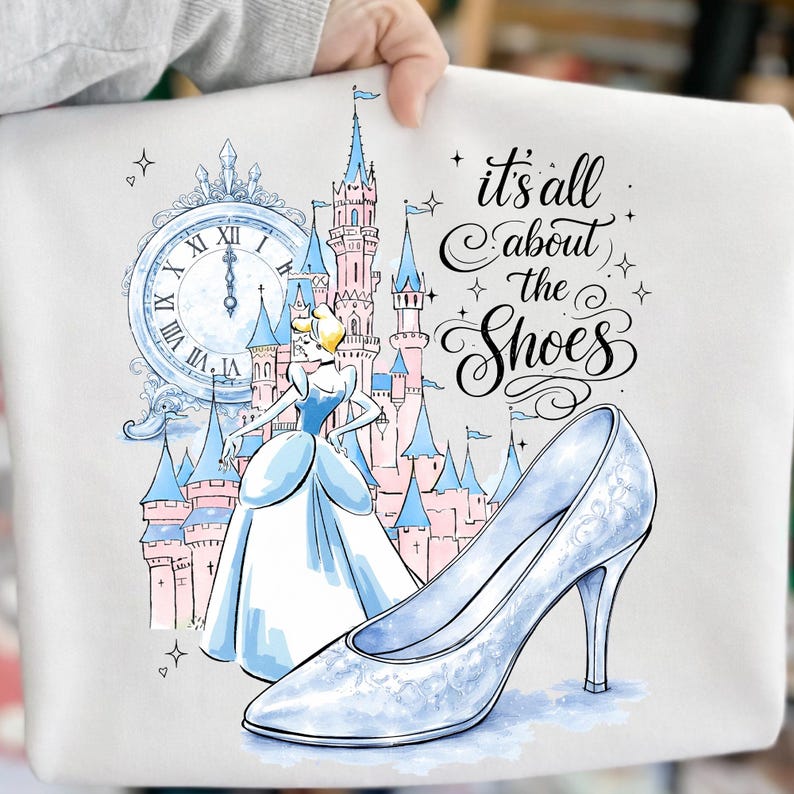 May include: A white graphic featuring Cinderella, a castle, and a glass slipper. The text "it's all about the Shoes" is written in cursive. The illustration is in shades of blue, pink, and white.