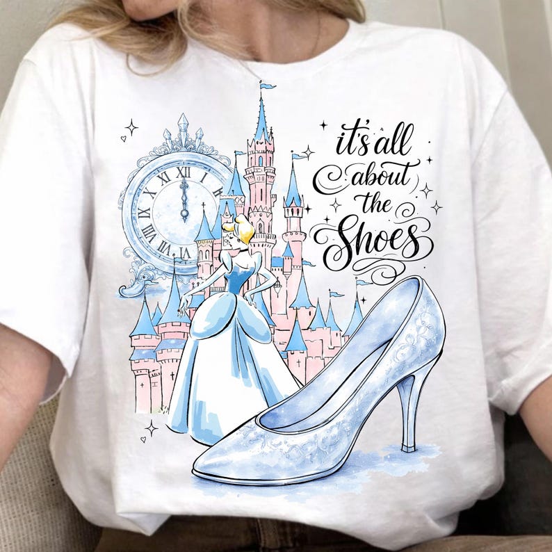 May include: White t-shirt featuring a Cinderella-themed design. The graphic includes a light blue high-heeled shoe, a castle, a clock, and the text "it's all about the Shoes". The design is in a watercolor style.