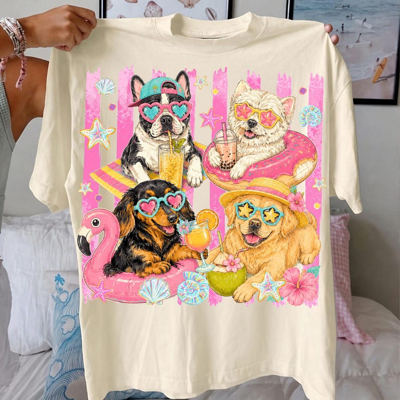 May include: Cream-colored t-shirt featuring a graphic of four dogs wearing sunglasses and enjoying tropical drinks and floats. The dogs are surrounded by pink stripes, seashells, and starfish, creating a fun, summer vibe.