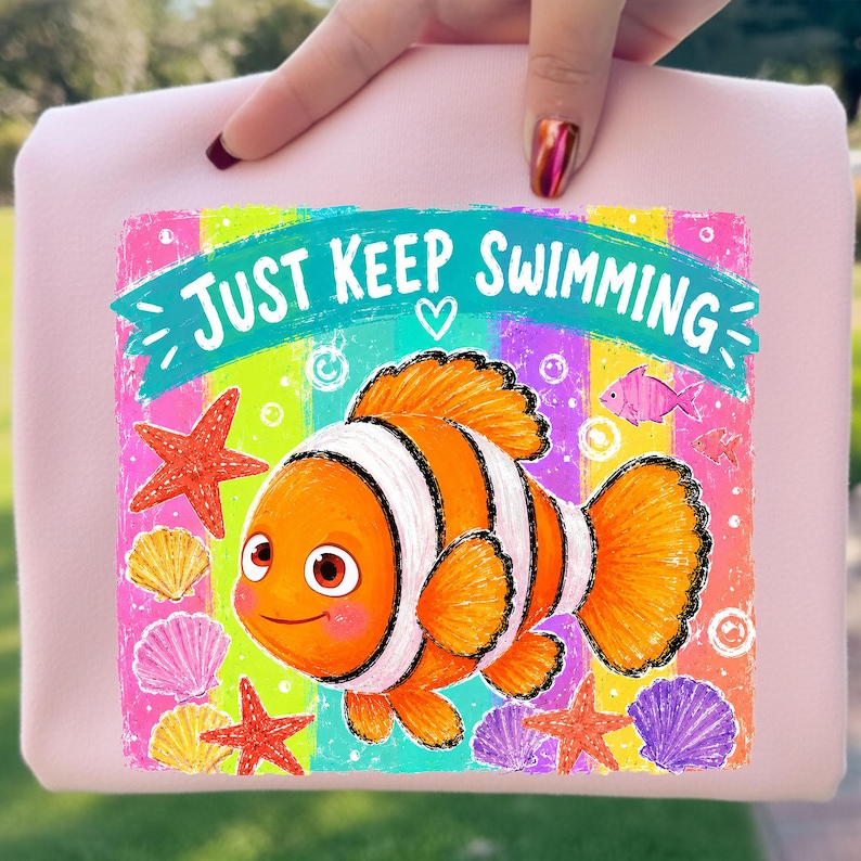 Może przedstawiać: Jasnor&oacute;żowa torba typu tote z kolorową grafiką. Przedstawia pomarańczowo-białą błazenka z napisem "JUST KEEP SWIMMING". Projekt zawiera rozgwiazdy, muszle i tęczowe tło.