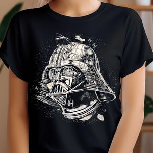 May include: Black t-shirt featuring a detailed white illustration of Darth Vader's helmet, incorporating elements of a cityscape and space battle. The design includes spaceships and a starry background, creating a unique graphic.