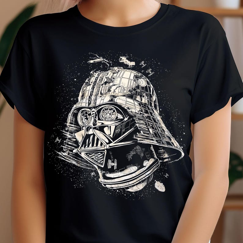 May include: Black t-shirt featuring a detailed white illustration of Darth Vader's helmet, incorporating elements of a cityscape and space battle. The design includes spaceships and a starry background, creating a unique graphic.