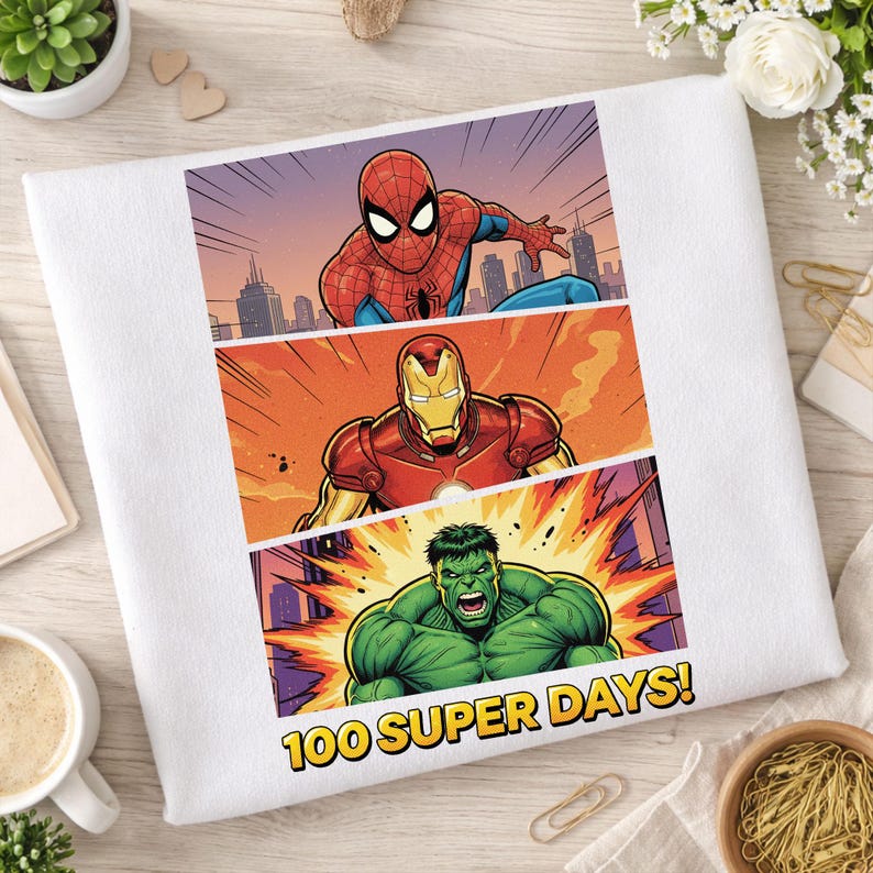 May include: White t-shirt featuring comic book panels of Spider-Man, Iron Man, and the Hulk. The design has a cityscape background and the text "100 SUPER DAYS!" in yellow. The artwork is in a vibrant, colorful style.