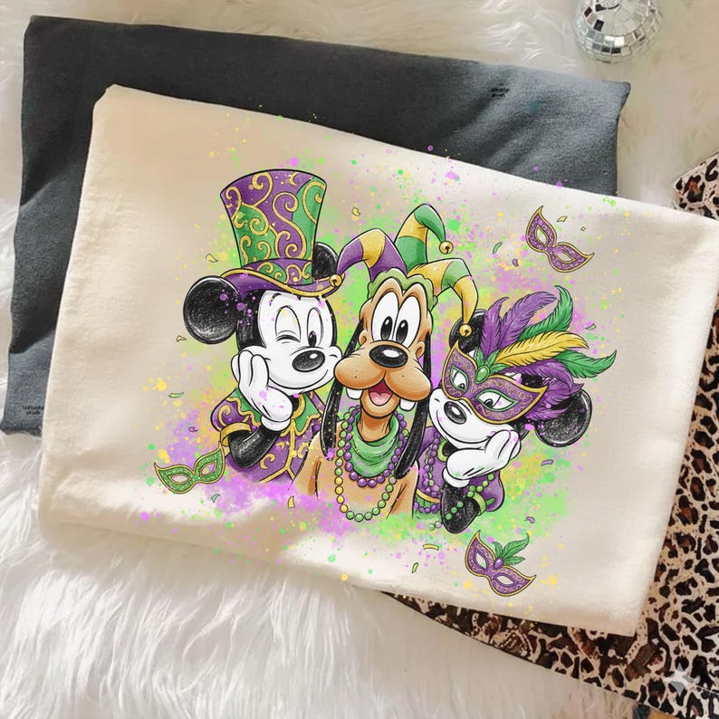 May include: A cream-colored pillowcase featuring a colorful illustration of Mickey Mouse, Goofy, and another Mickey Mouse character in Mardi Gras attire. The characters are wearing purple, green, and gold outfits and masks. The design includes confetti and decorative masks.