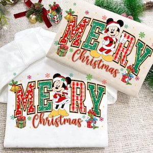 Puede incluir: Dos sudaderas con temática navideña. Una es blanca, la otra beige. Ambas presentan las palabras "MERRY Christmas" en rojo y verde, con personajes de Mickey y Minnie Mouse vestidos de Papá Noel. También se incluyen regalos y copos de nieve.