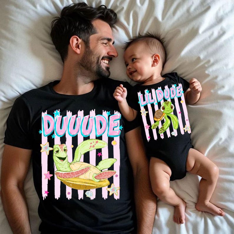 May include: Matching black t-shirts and onesie with a cartoon turtle design. The adult shirt says "DUUUUDE" in pink and blue, while the baby's onesie says "LIL DUDE". Both feature a green turtle on a yellow base with pink and white striped backgrounds.