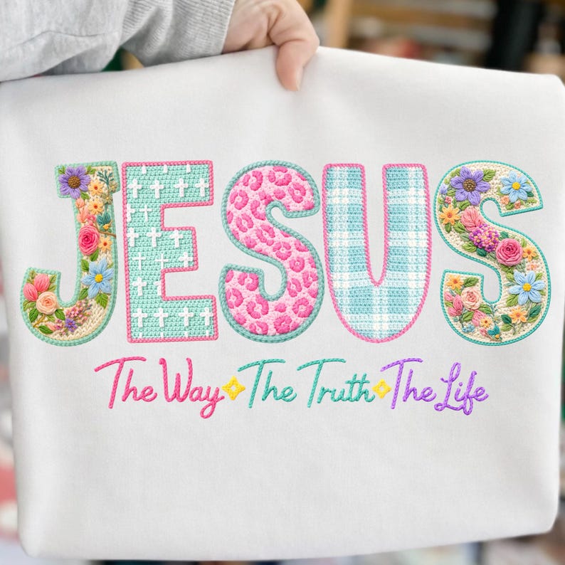Puede incluir: Sudadera blanca con la palabra "JESUS" bordada en dise&ntilde;os coloridos, florales y estampados. Debajo de la palabra "JESUS" est&aacute; el texto bordado "The Way The Truth The Life".