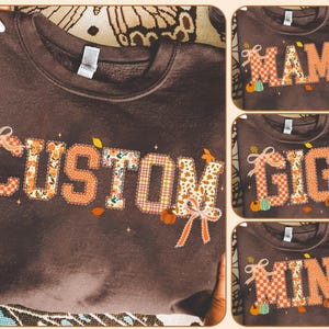 May include: A brown sweatshirt with the word "CUSTOM" in patchwork letters, decorated with pumpkins and bows. Additional sweatshirts feature the words "MAMA", "GIGI", and "MINI" in similar designs. The sweatshirts are held by hands.