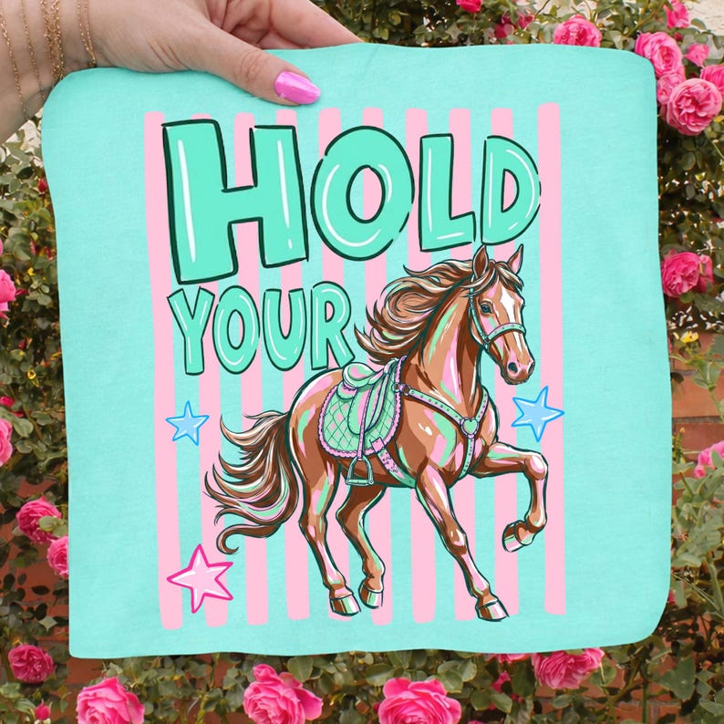 May include: A light blue fabric with the words "HOLD YOUR" in large, turquoise letters. A brown horse with a saddle and bridle is depicted below the text, with pink and turquoise stars and stripes.