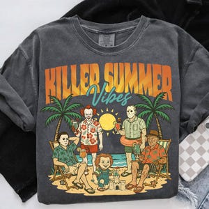May include: Dark gray sweatshirt with the text "KILLER SUMMER Vibes" in orange and blue. The graphic features cartoon characters on a beach with palm trees, a sun, and cocktails. The characters include Pennywise, Jason Voorhees, Michael Myers, Chucky, and Freddy Krueger.
