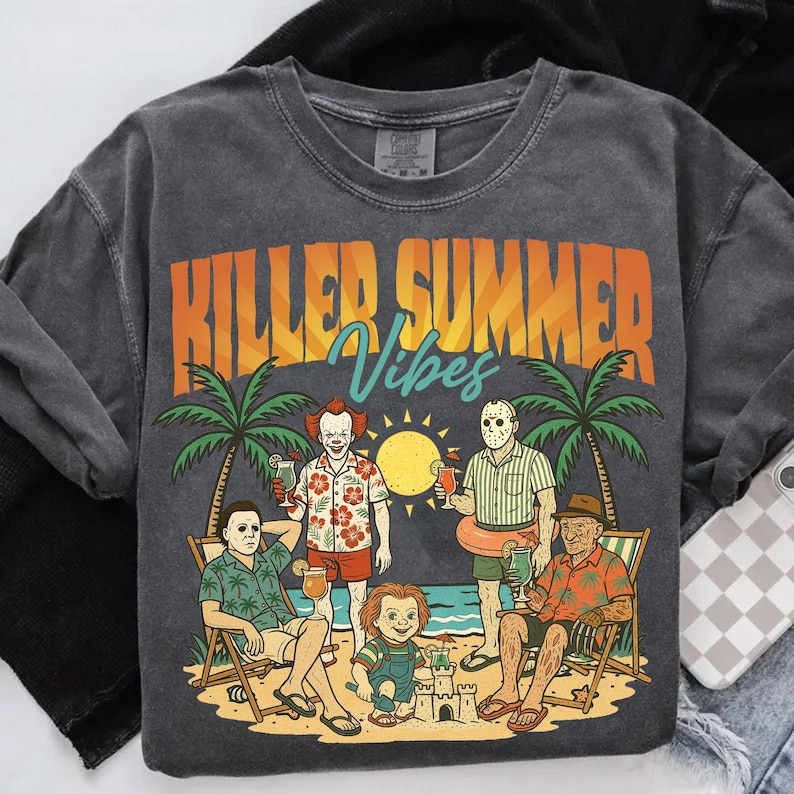 May include: Dark gray sweatshirt with the text "KILLER SUMMER Vibes" in orange and blue. The graphic features cartoon characters on a beach with palm trees, a sun, and cocktails. The characters include Pennywise, Jason Voorhees, Michael Myers, Chucky, and Freddy Krueger.