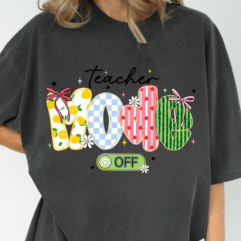 Op de afbeelding: Donkergrijs T-shirt met de tekst "Teacher Mode Off" in een kleurrijk, grillig ontwerp. Het woord "Mom" is creatief ontworpen met citroen-, geruite, aardbei- en watermeloenpatronen. Het shirt heeft een relaxte pasvorm.