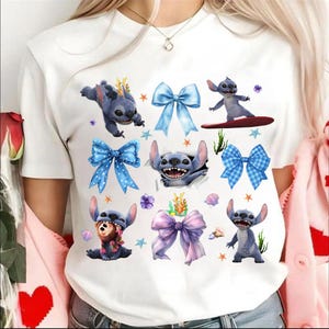 May include: White t-shirt featuring multiple cartoon images of Stitch, the blue alien character, along with blue bows, starfish, and other decorative elements. The design includes Stitch in various poses, adding a playful touch to the shirt.