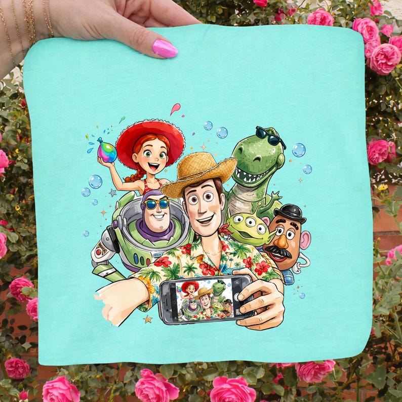 May include: A light blue square towel featuring a colorful illustration of characters from the Toy Story movie franchise taking a selfie. The characters include Woody, Buzz Lightyear, Rex, and others. The towel is held by a person.