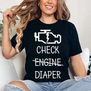 May include: Black t-shirt with a white check engine light icon and the text "CHECK ENGINE DIAPER" with the word "ENGINE" crossed out.