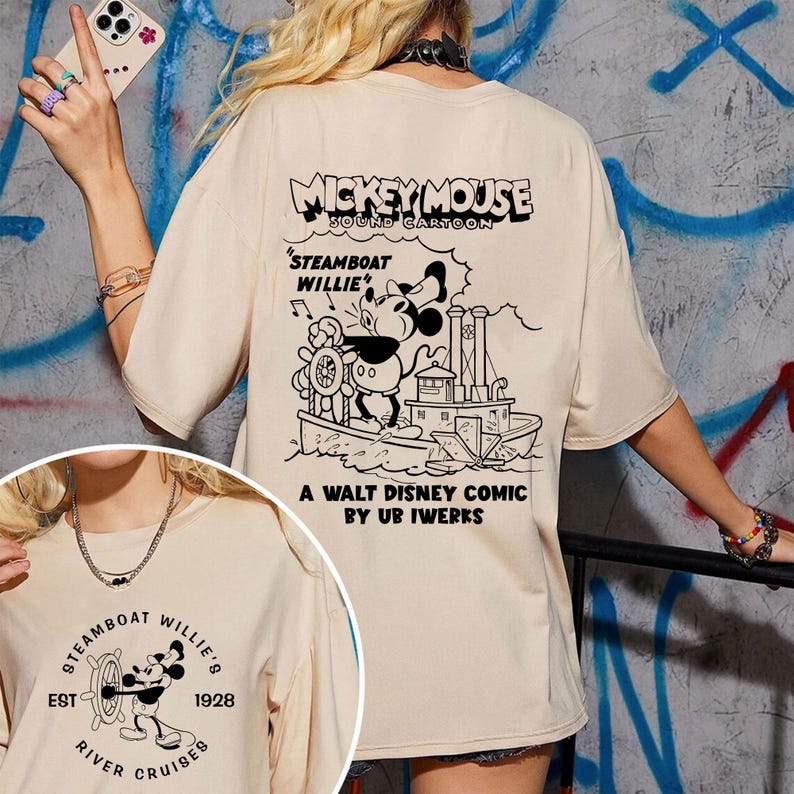 May include: A beige t-shirt featuring a black and white graphic of Mickey Mouse on a steamboat. The text "Mickey Mouse Sound Cartoon" and "Steamboat Willie" is printed on the shirt. The text "A Walt Disney Comic by Ub Iwerks" is printed on the bottom of the shirt.