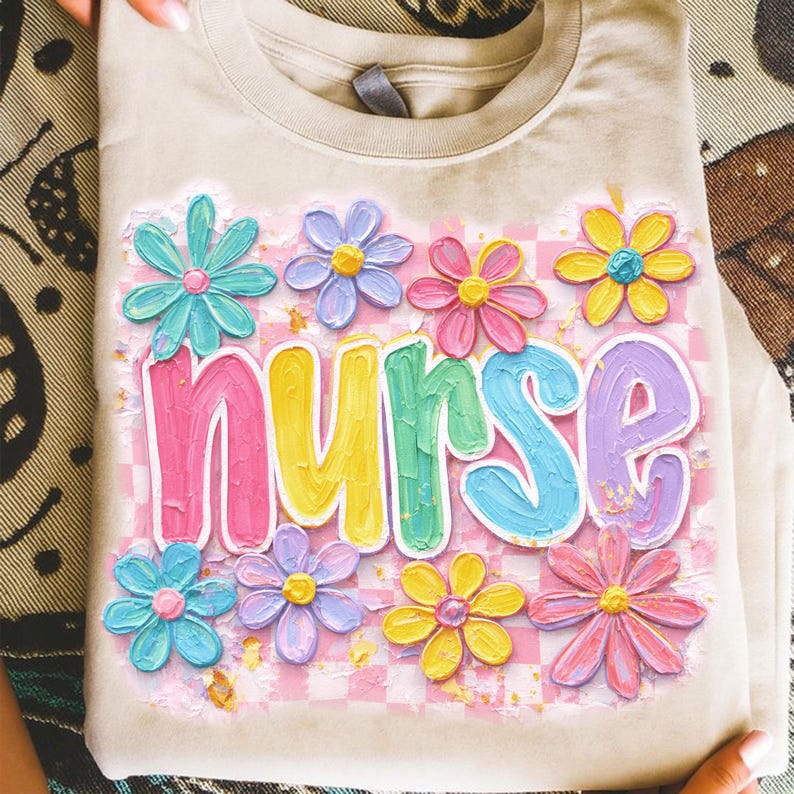 May include: A beige t-shirt with a colorful floral design and the word "nurse" in large, pastel letters. The flowers are in shades of blue, pink, yellow, and purple, set against a pink and white checkered background.