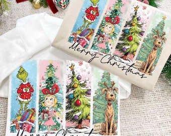 May include: Two white sweatshirts with a colorful Christmas-themed graphic. The design features characters and elements from a holiday story, including a green character in a red suit, a girl, Christmas trees, and a dog. The words "Merry Christmas" are written in a script font.