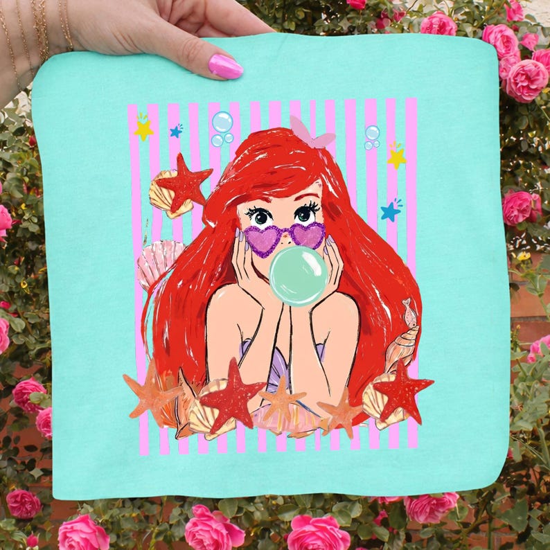 May include: A teal square with a cartoon mermaid illustration. The mermaid has red hair, heart-shaped sunglasses, and is blowing a bubble. The background features pink stripes, starfish, seashells, and bubbles.