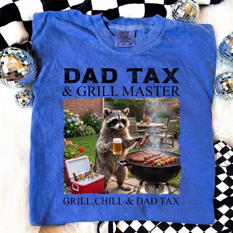 May include: Blue Comfort Colors sweatshirt with the text "DAD TAX & GRILL MASTER" and a graphic of a raccoon grilling. The raccoon is holding a beer and a sausage. The text "GRILL, CHILL & DAD TAX" is also on the shirt.